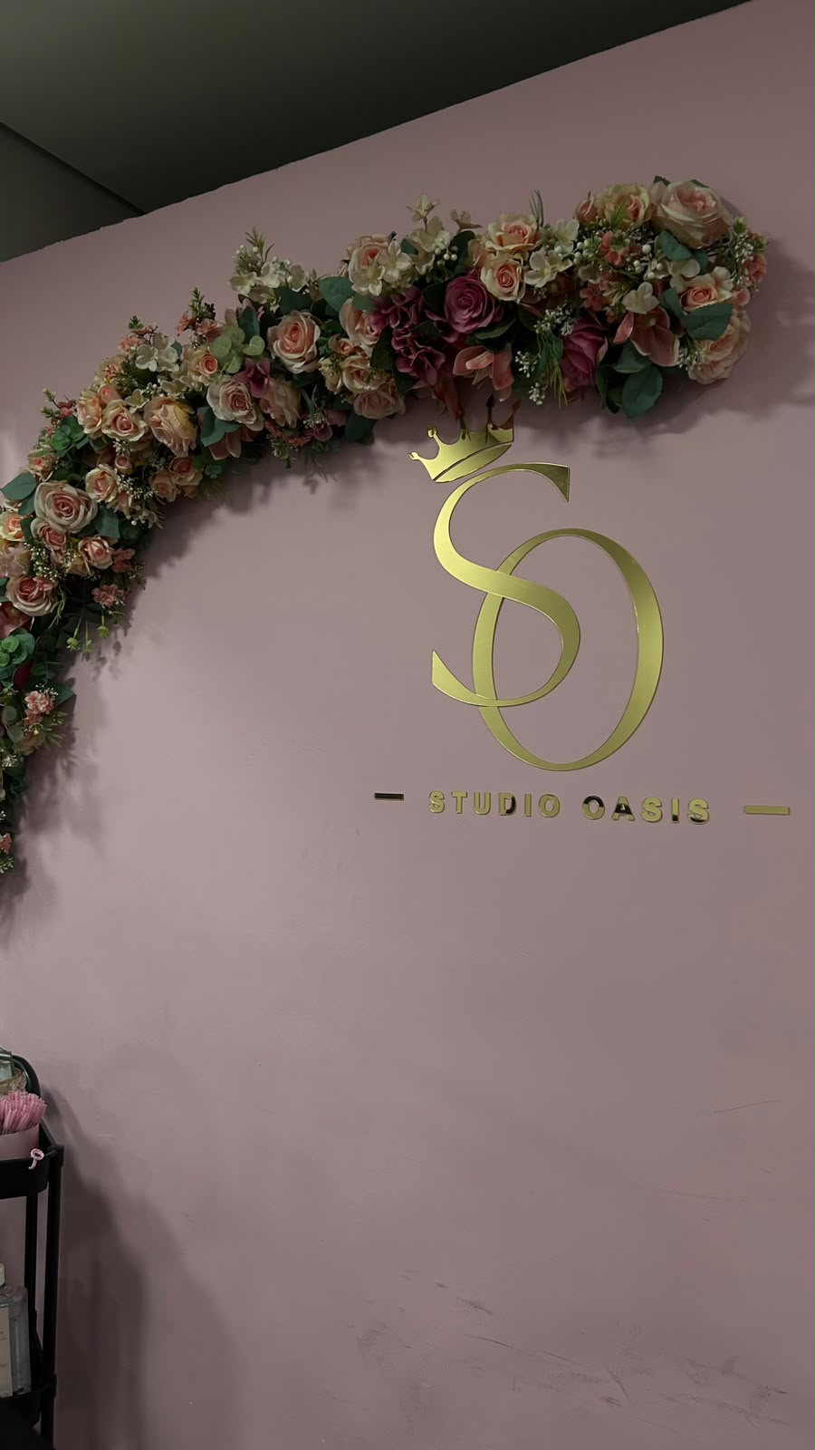 Parede com o logo dourado do Studio Oasis e arco de flores